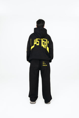 Person wearing a black hoodie and pants with yellow text on a white background